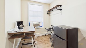 A compact kitchen with a refrigerator, a coffee maker, a window with blinds, and a wall-mounted shelf. - Rally Point Inn & Pub (Foxborough)