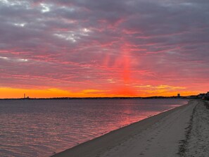 Une plage au coucher du soleil, avec une eau calme et une côte lointaine.