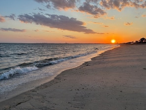 A beach with waves, a sunset, and buildings in the distance. - Private Beachfront Cottage for 2—Spacious Deck on the Water, Breathtaking Views! (Truro)