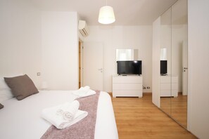 Ein modernes Hotelzimmer mit Bett, Fernseher auf einer weißen Kommode, einem Spiegel und einem Kleiderschrank.