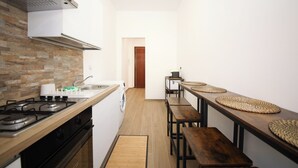 A narrow kitchen with a stove, sink, and a washing machine. There are wooden benches and woven placemats along the counter. - Domus Alexander by Ghor (Rome)