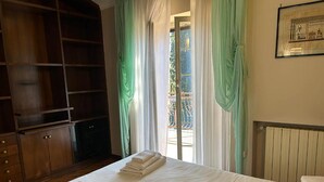A hotel room with a bed, a wooden wardrobe, a radiator, and a balcony with green curtains. - Villa Visconti by Ghor (Rome)