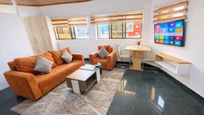 Un espacio de oficina moderno con dos sofás naranja, una mesa baja, una pequeña mesa de madera y un televisor en la pared.