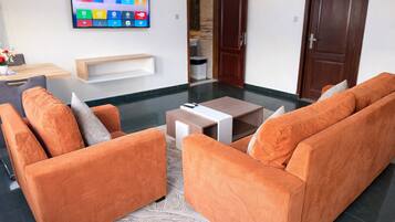 A living room with orange sofas, a coffee table, and a flat-screen TV mounted on the wall.
