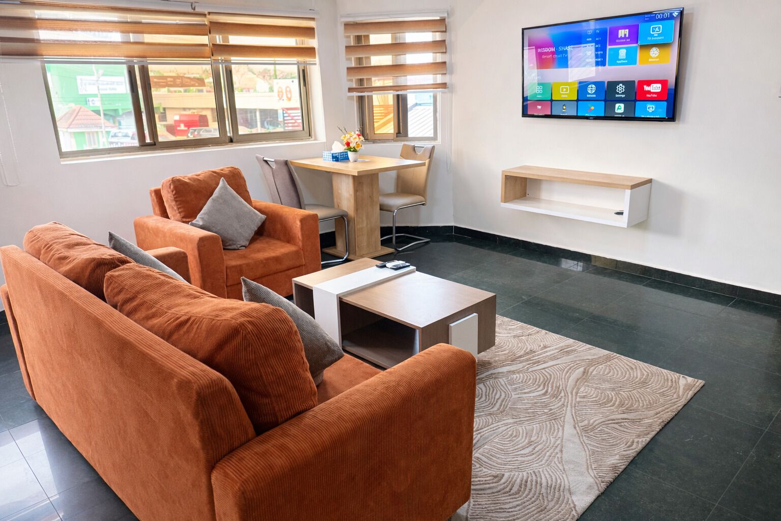 A modern living room with orange sofas, a wooden coffee table, and a TV mounted on the wall.