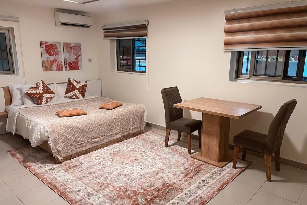 Ein Schlafzimmer mit einem Bett, einem Schreibtisch, zwei Stühlen, einem Teppich und Bildern an den Wänden.