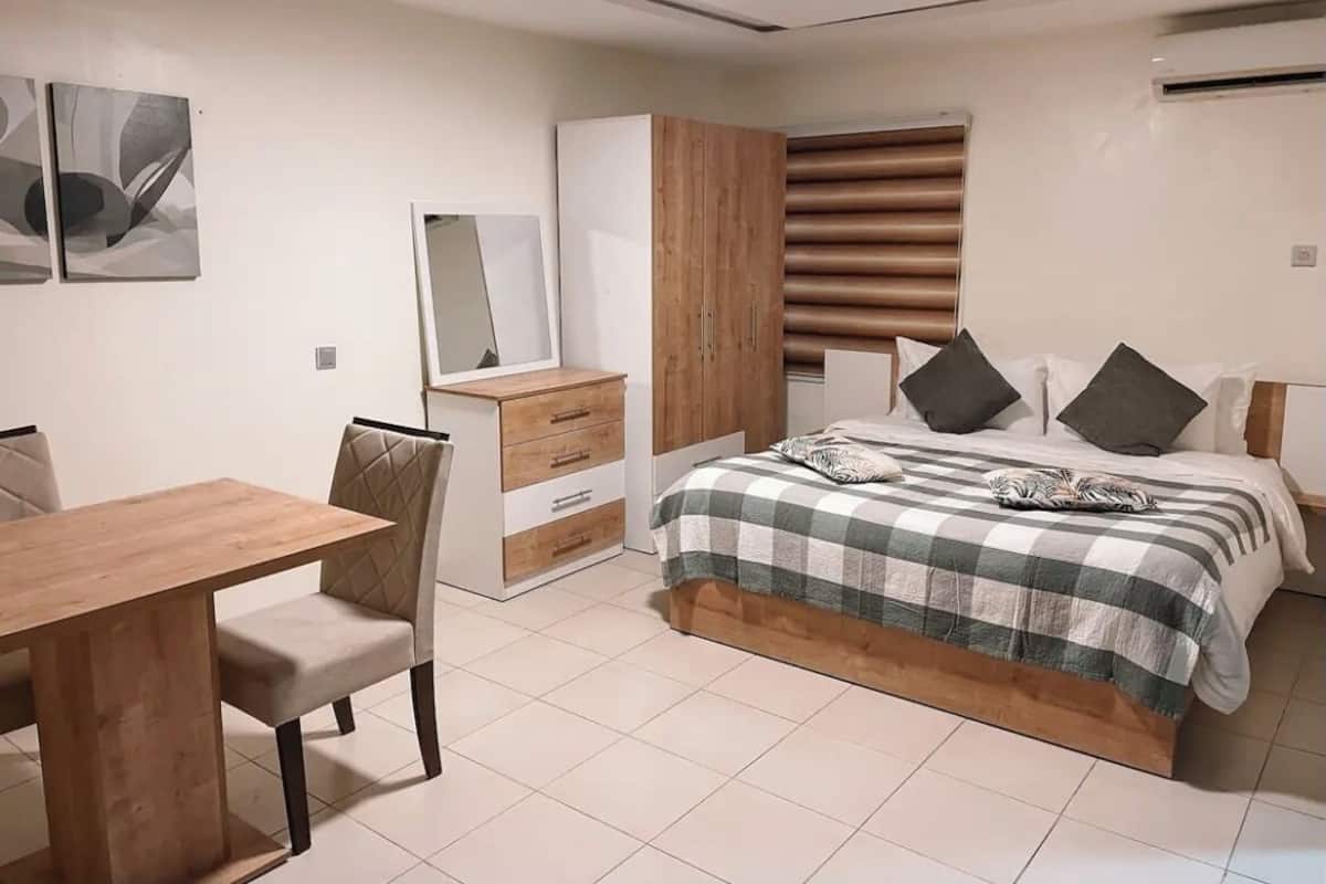 Ein Schlafzimmer mit Bett, Schreibtisch, Stuhl, Kleiderschrank und einem Fenster mit Jalousien.