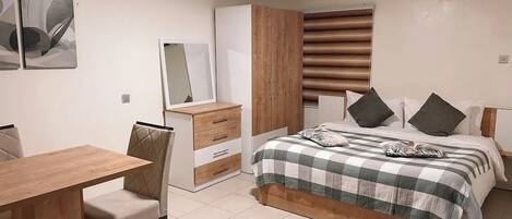Un dormitorio con cama, escritorio, silla, armario y ventana con persianas.