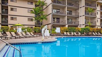 A swimming pool with lounge chairs and umbrellas, surrounded by a multi-story building with balconies.