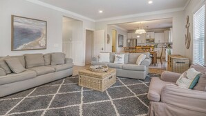 A spacious living room with two sofas, a coffee table, and a rug. A kitchen and dining area are visible in the background. - Bridgewater Cottage- Close to Beach, 6 Bedrooms. (South Haven)