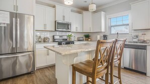 A modern kitchen with white cabinets, stainless steel appliances, a central island with bar stools, and pendant lighting. - Bridgewater Cottage- Close to Beach, 6 Bedrooms. (South Haven)