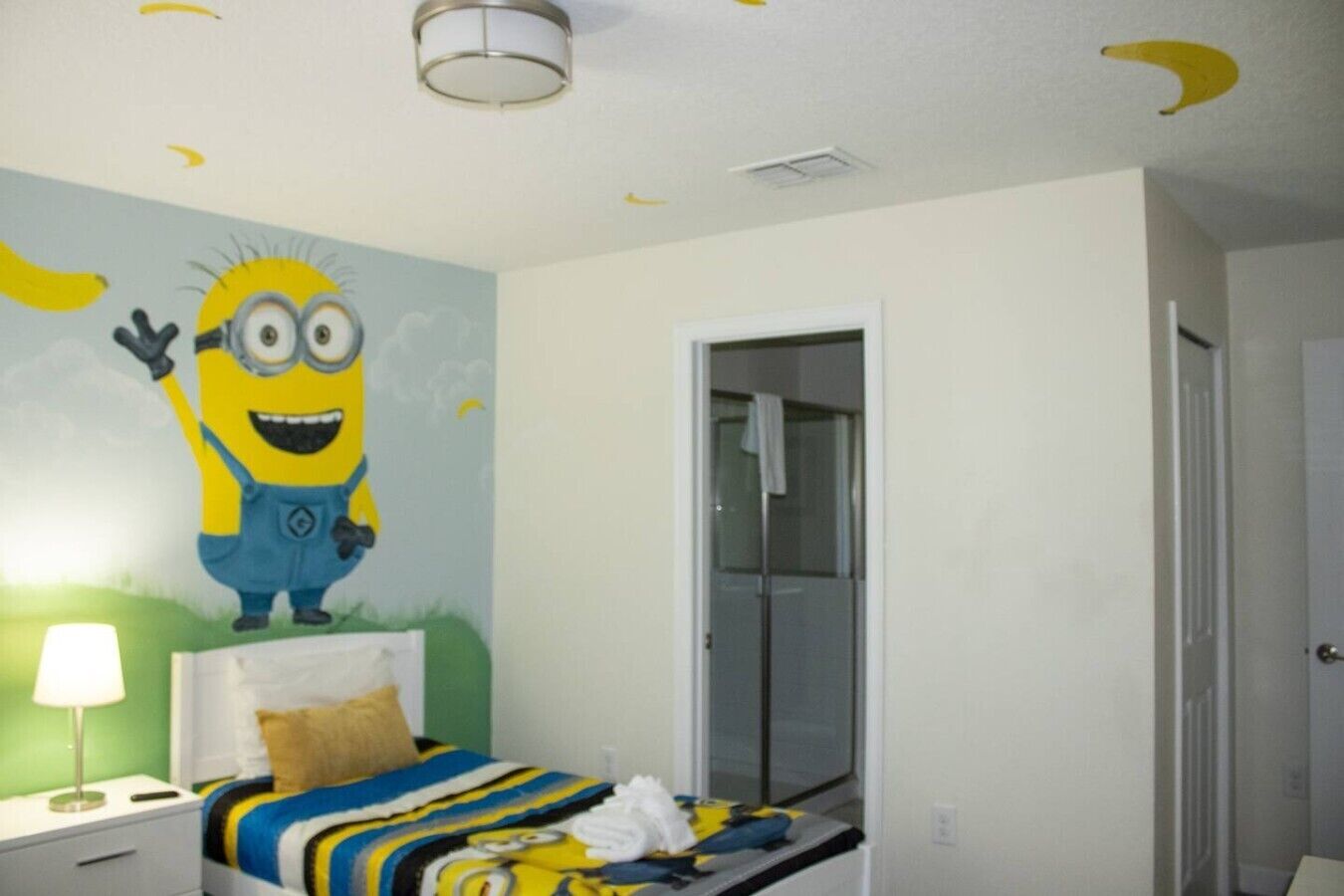 A bedroom with a bed, a nightstand, a wall mural, a door, and a ceiling light fixture.