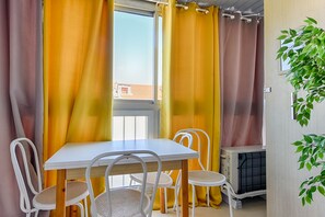 A room with a white table and chairs, yellow curtains, and a potted plant. - Le Festif studio avec loggia au Carré d'Or (Cannes)