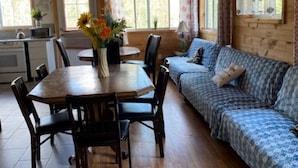 L’intérieur chaleureux d’un chalet avec une table à manger en bois, des chaises, un canapé et un coin cuisine.