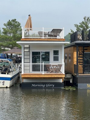 A houseboat named 'Morning Glory' docked at a marina with a wooden deck and a small balcony.