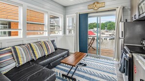 A modern kitchen with a built-in oven and microwave, a black leather sofa with striped pillows, and a view of the deck through the glass door. - Morning Glory - Floating Cottage (TFC#3) - Resort (South Haven)