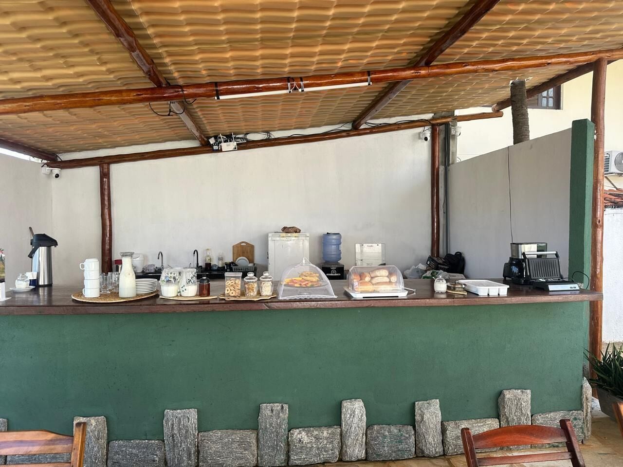A covered outdoor area with a counter displaying breakfast items, a coffee machine, and a water dispenser.