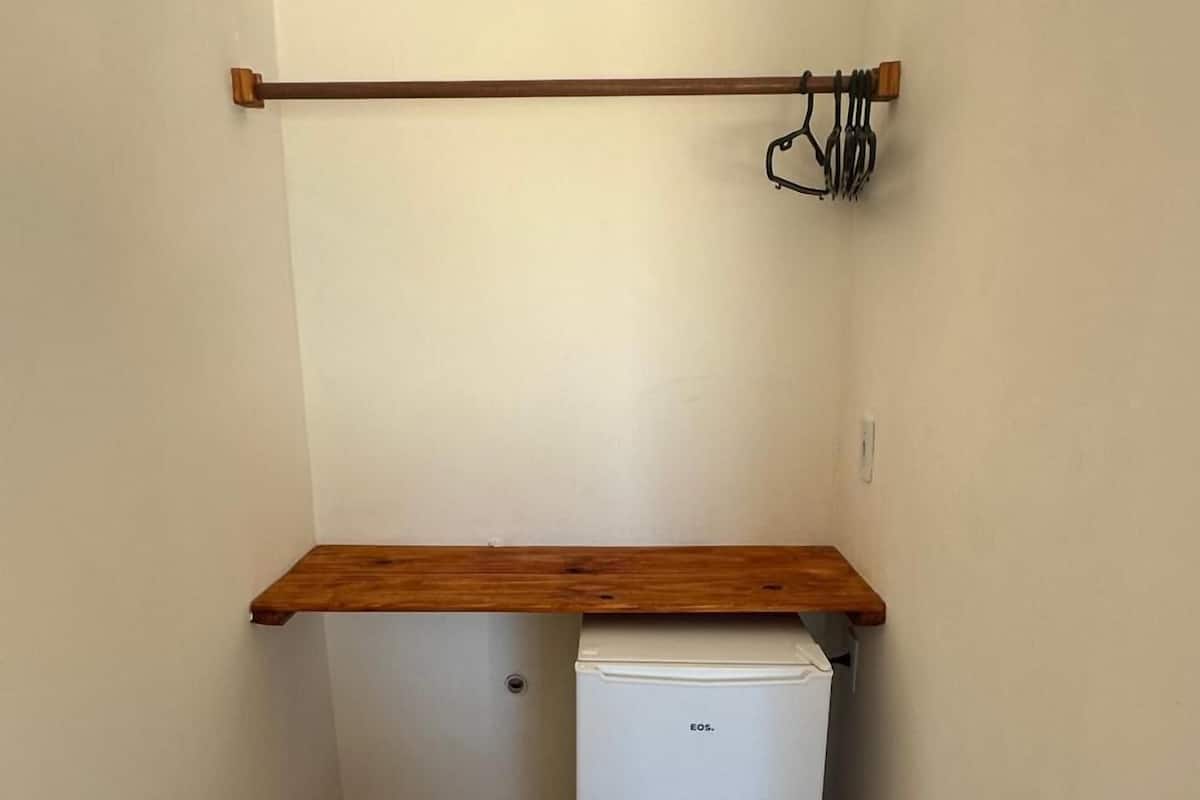 Een kleine, smalle kamer met een witte koelkast, een houten plank en een wandlamp.