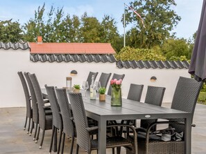 Un espace de restauration en plein air, avec une table et des chaises, entouré d’un mur blanc surmonté d’un toit en tuiles.