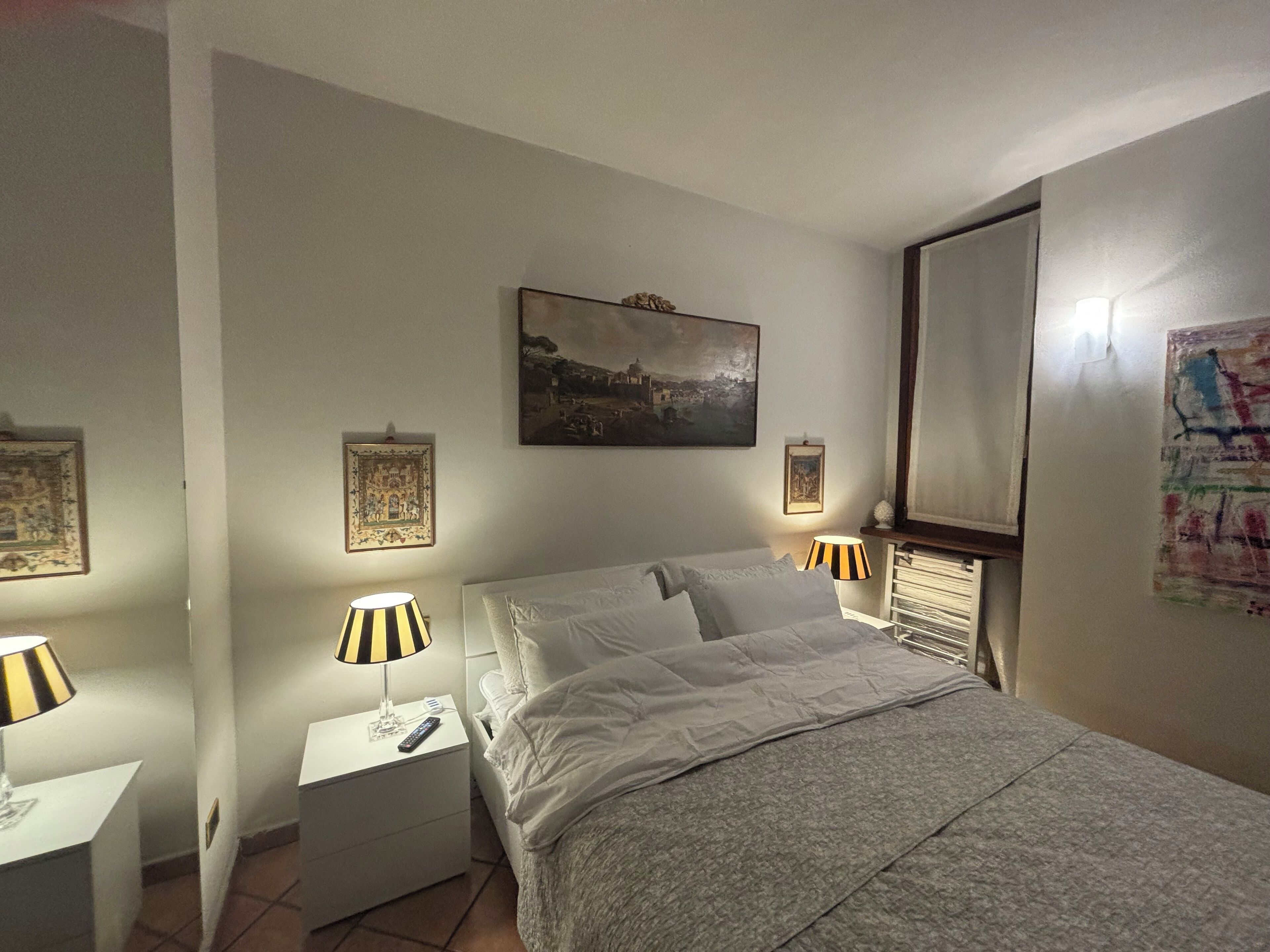 A bedroom with a bed, two bedside tables with lamps, a nightstand, and wall art.