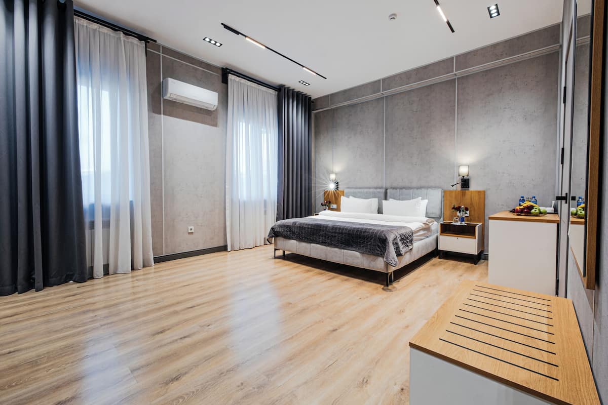 A modern hotel room with a large bed, bedside tables, a wooden bench, and a wardrobe.