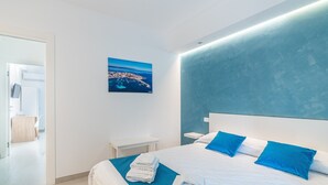 A modern hotel room with a large bed, a nightstand, a small table, and a painting on the wall. - Aura B&B - Quadruple Room Bed and Breakfast (Pachino)