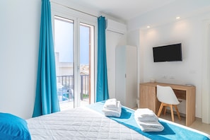 Una habitación de hotel con cama, escritorio, televisor y balcón con cortinas.
