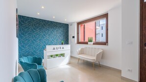 Un salón moderno con sillas color turquesa, un sofá blanco, una pared con estampado azul y una ventana con vistas.