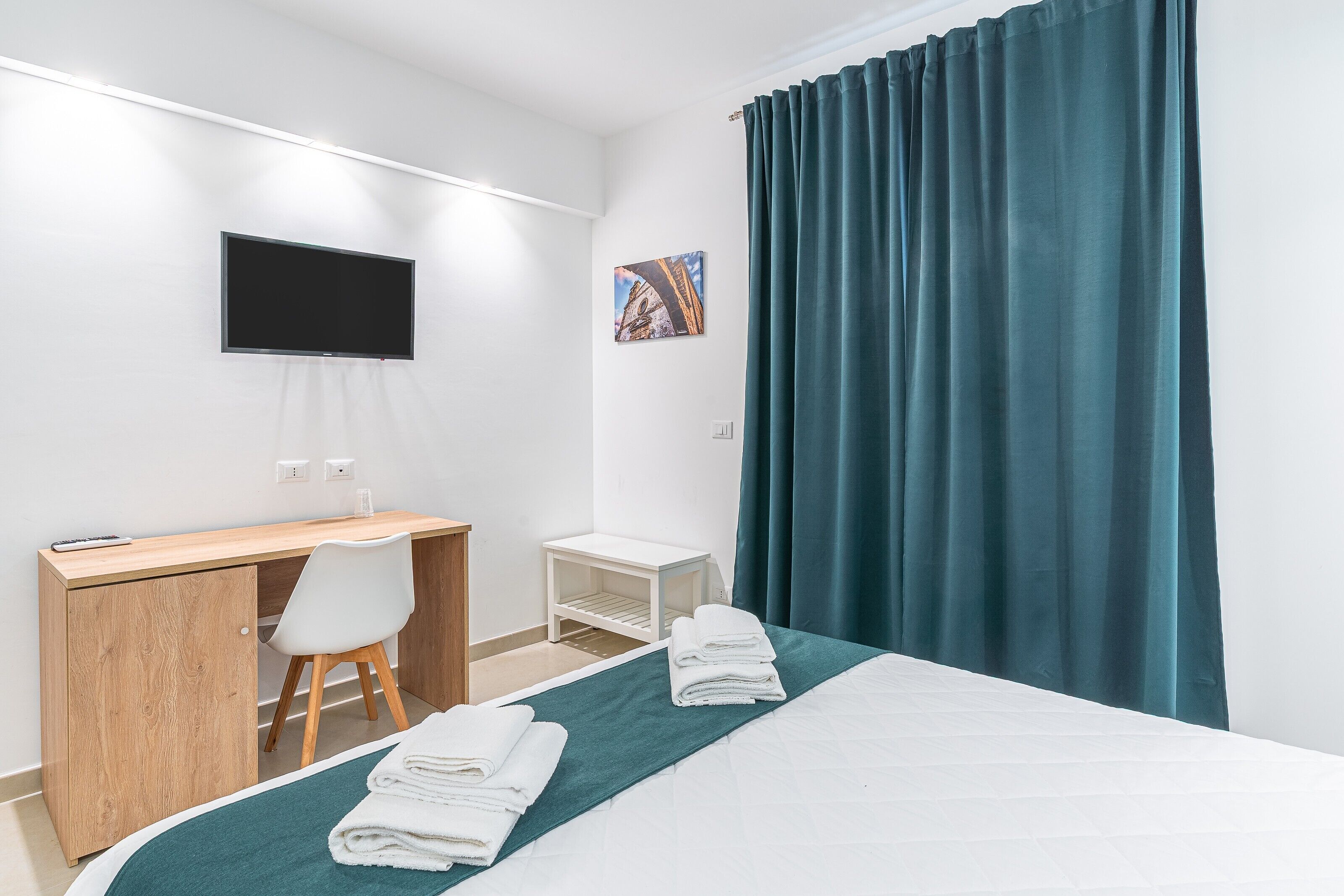Habitación de hotel con cama, escritorio, silla, televisor y una mesita.
