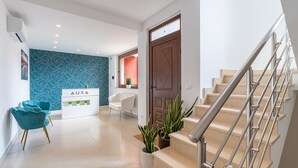 Un interior moderno con una escalera, una recepción con el rótulo 'AURA' y una pared azul estampada.