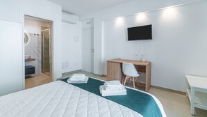 Una habitación de hotel moderna con cama, escritorio, silla, televisor y zona de ducha.