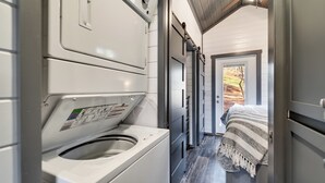 A laundry room with a washing machine, a dryer, and a door leading to a bedroom with a bed and a view of trees. - Escape to your own Tiny Slice of Heaven in Franklin, N (Franklin)