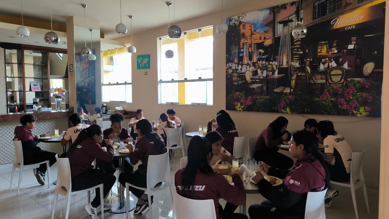 A restaurant with tables and chairs, a mural on the wall, and a window with natural light.