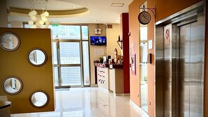 Eine Hotelhalle mit einer Rezeption, einer Uhr und einem großen Fenster mit Jalousien.