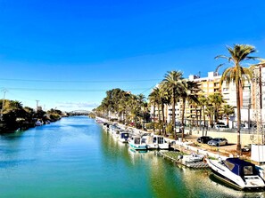 A canal with boats docked on the right, lined with palm trees and buildings.