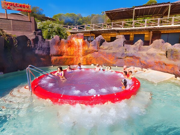 A pool with a red border, surrounded by rocky formations and a wooden structure in the background.
