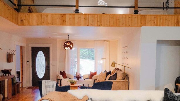 A spacious living area with a high wooden ceiling, a cozy sofa set, a dining table, and a staircase leading to an upper level. - The 312 House A Boho Retreat Hocking Hills (Logan)