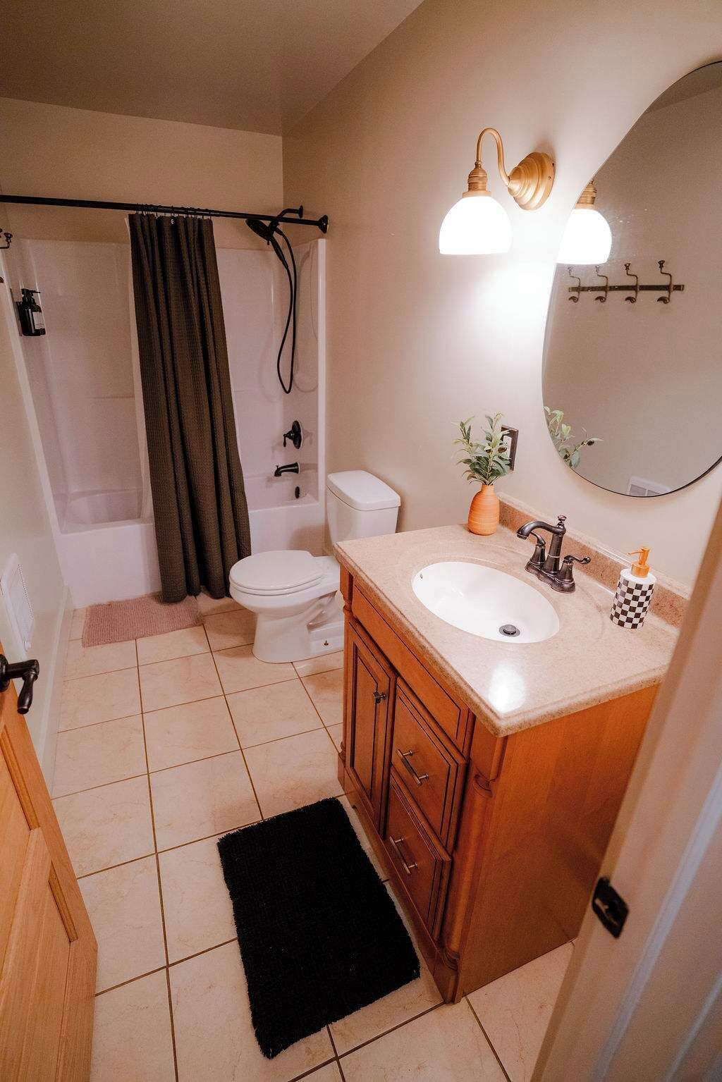 Une salle de bain avec des toilettes, un lavabo et une douche. Il y a un tapis noir sur le sol et une plante sur le comptoir du lavabo.