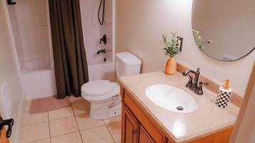 Une salle de bain avec des toilettes, un lavabo et une douche. Il y a un tapis noir sur le sol et une plante sur le comptoir du lavabo.