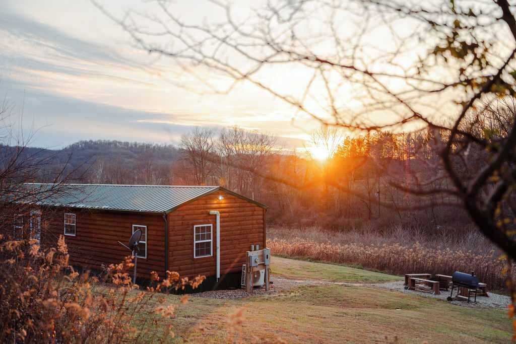Une cabane rustique avec un toit en métal, une antenne parabolique et un petit espace extérieur aménagé pour s’asseoir.