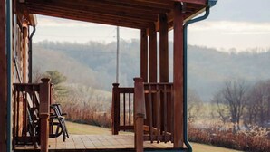 Una terraza de madera con un espacio de estar cubierto, una escalera que sube y vistas a un paisaje montañoso.
