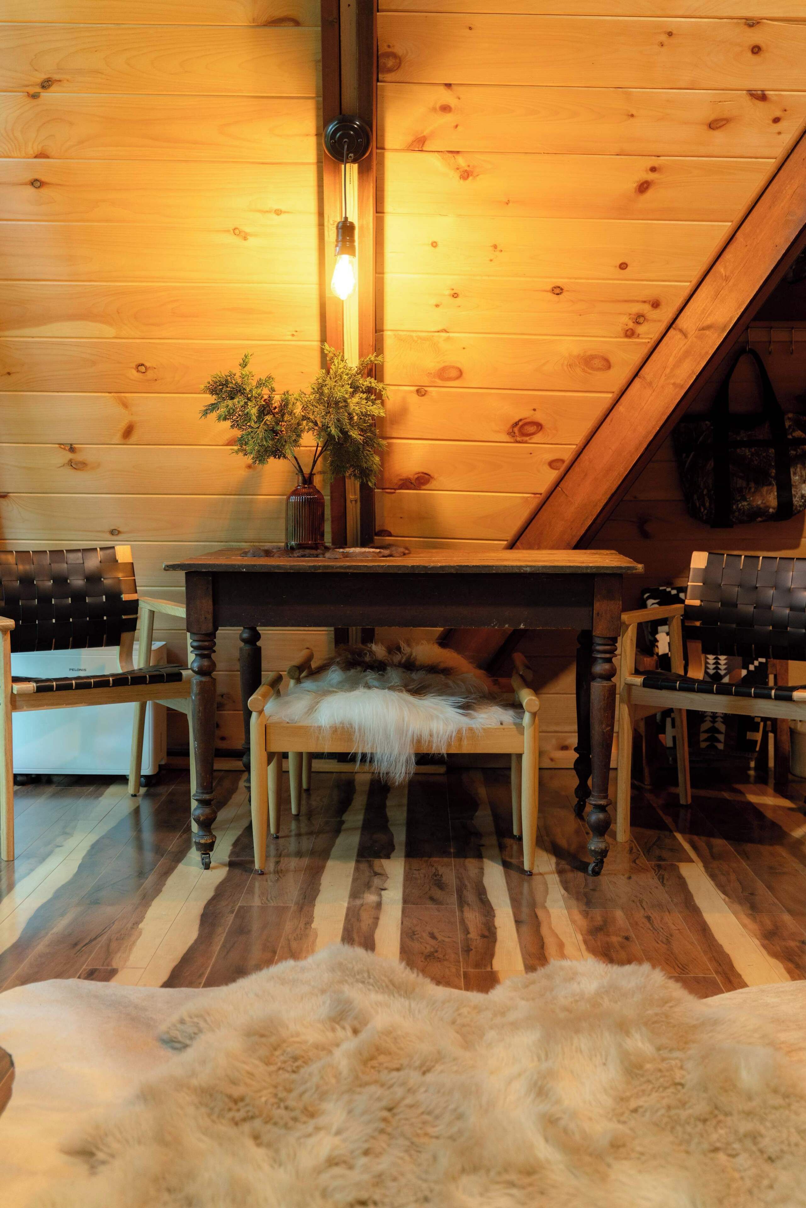 A wooden interior with a table, chairs, a bench, and a fur rug.
