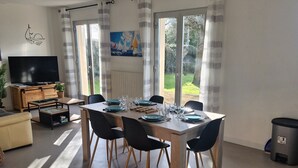 Een zithoek met een tafel voor vier personen, een bank, een televisie en een raam met gordijnen.
