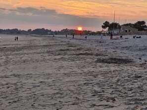 A beach with people walking and sitting, a sunset in the background, and a few structures in the distance. - Holiday Home “Ker Blein” with Sea View, Terrace and Wi-Fi (Sarzeau)