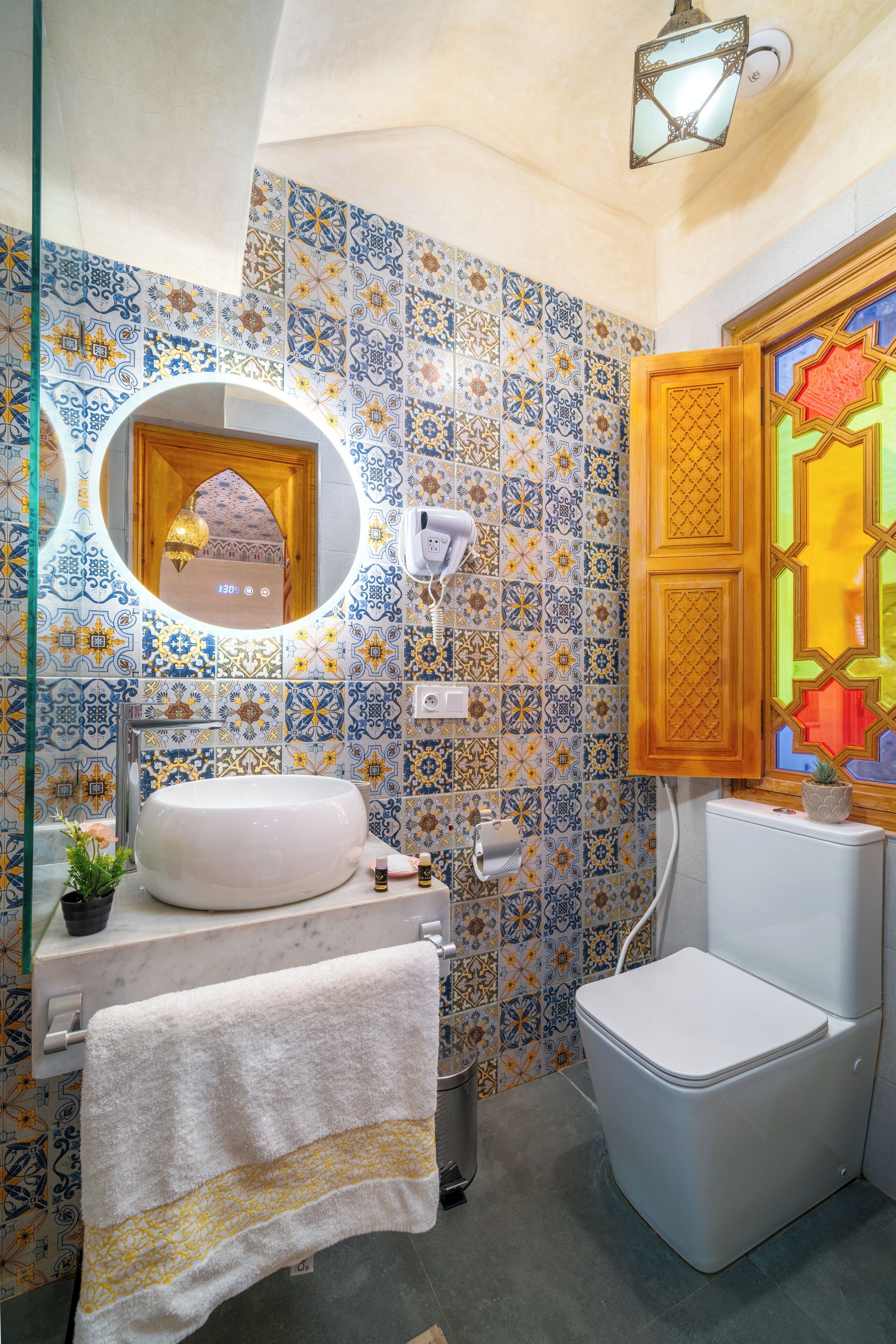 A bathroom with a white sink, a toilet, a mirror, and a patterned tile wall.