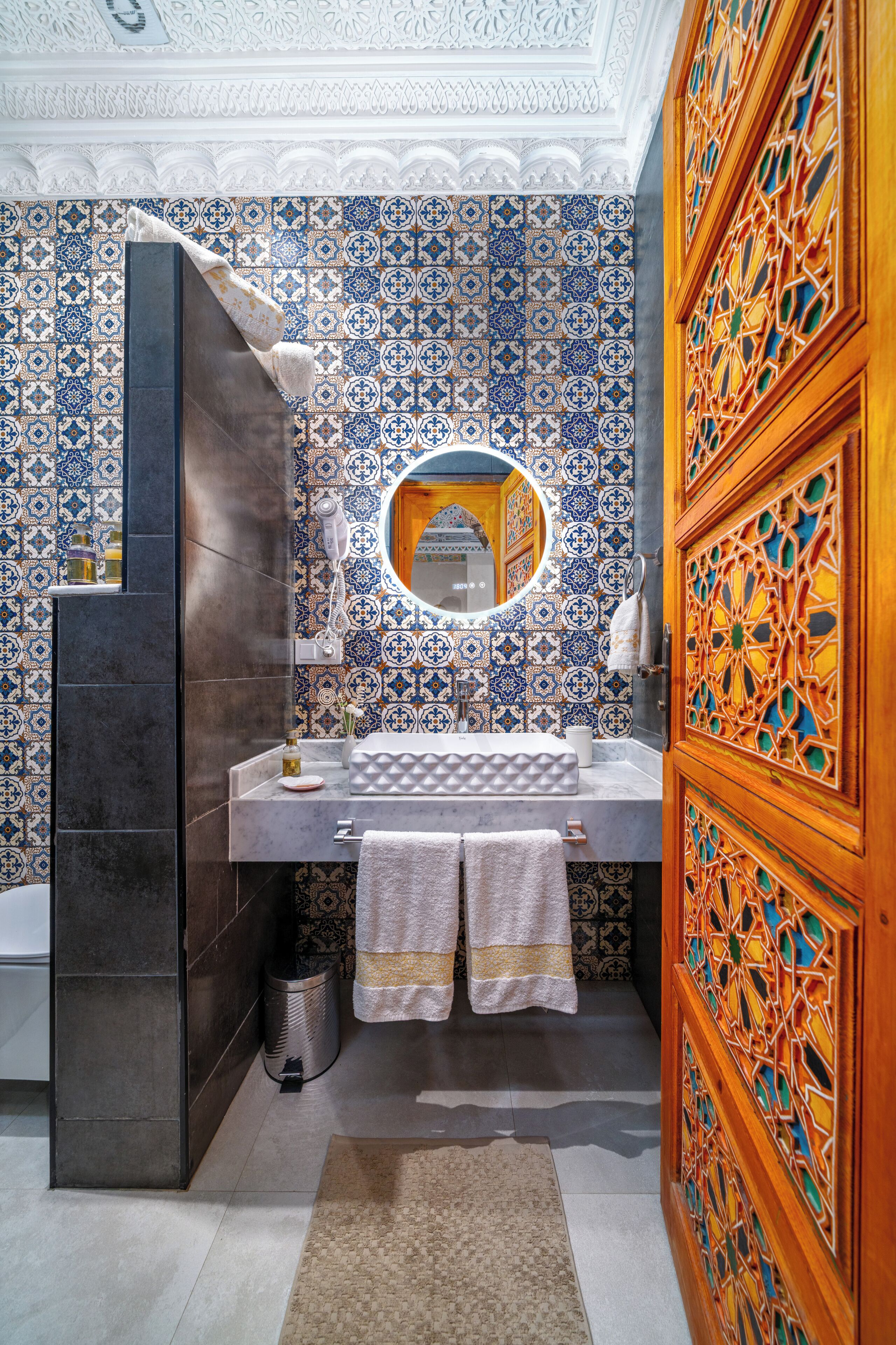 A bathroom with a tiled wall, a mirror, a sink, and a towel rack.