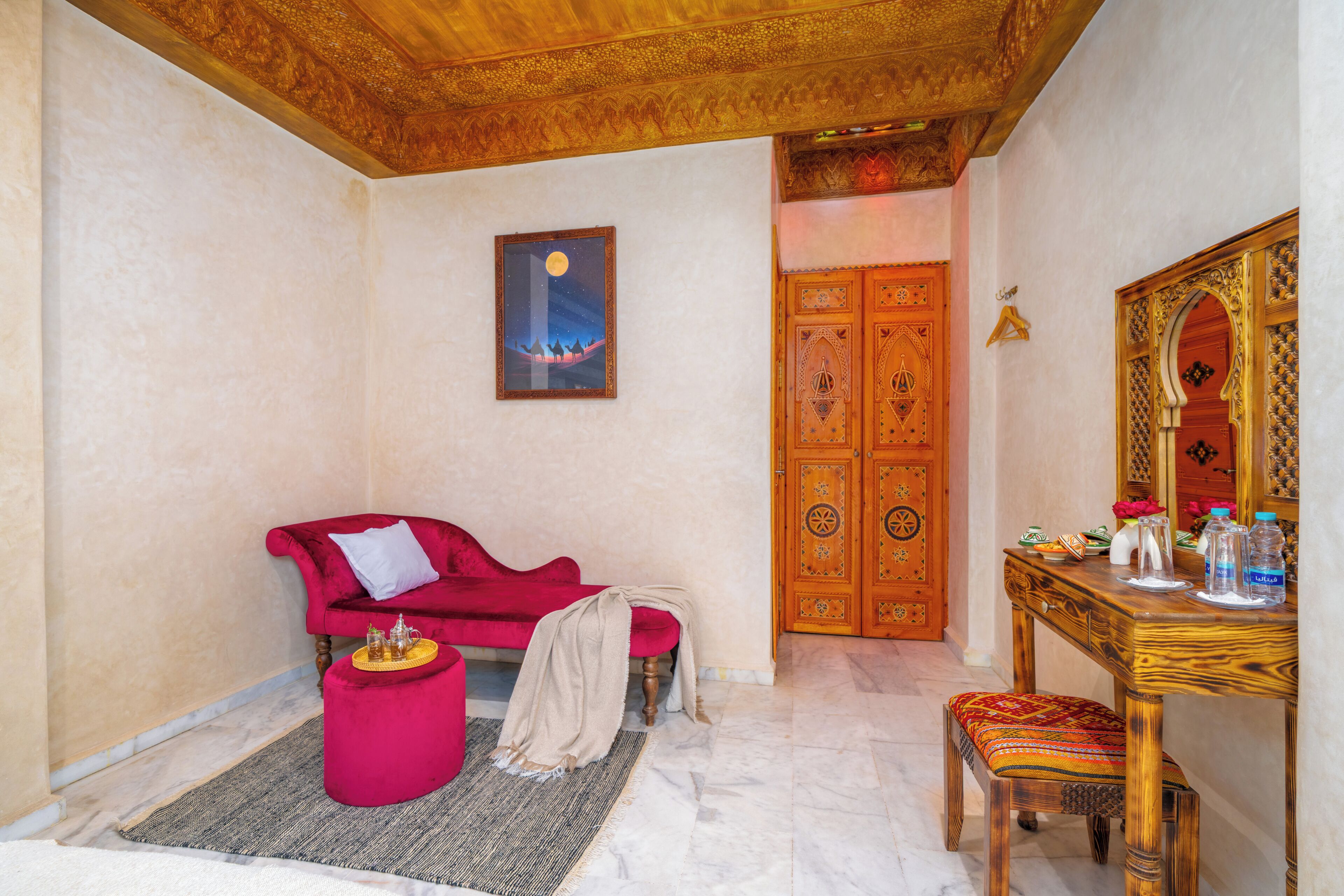 Una habitación con un sofá rojo, una mesa de madera con botellas, un espejo y una puerta tradicional.