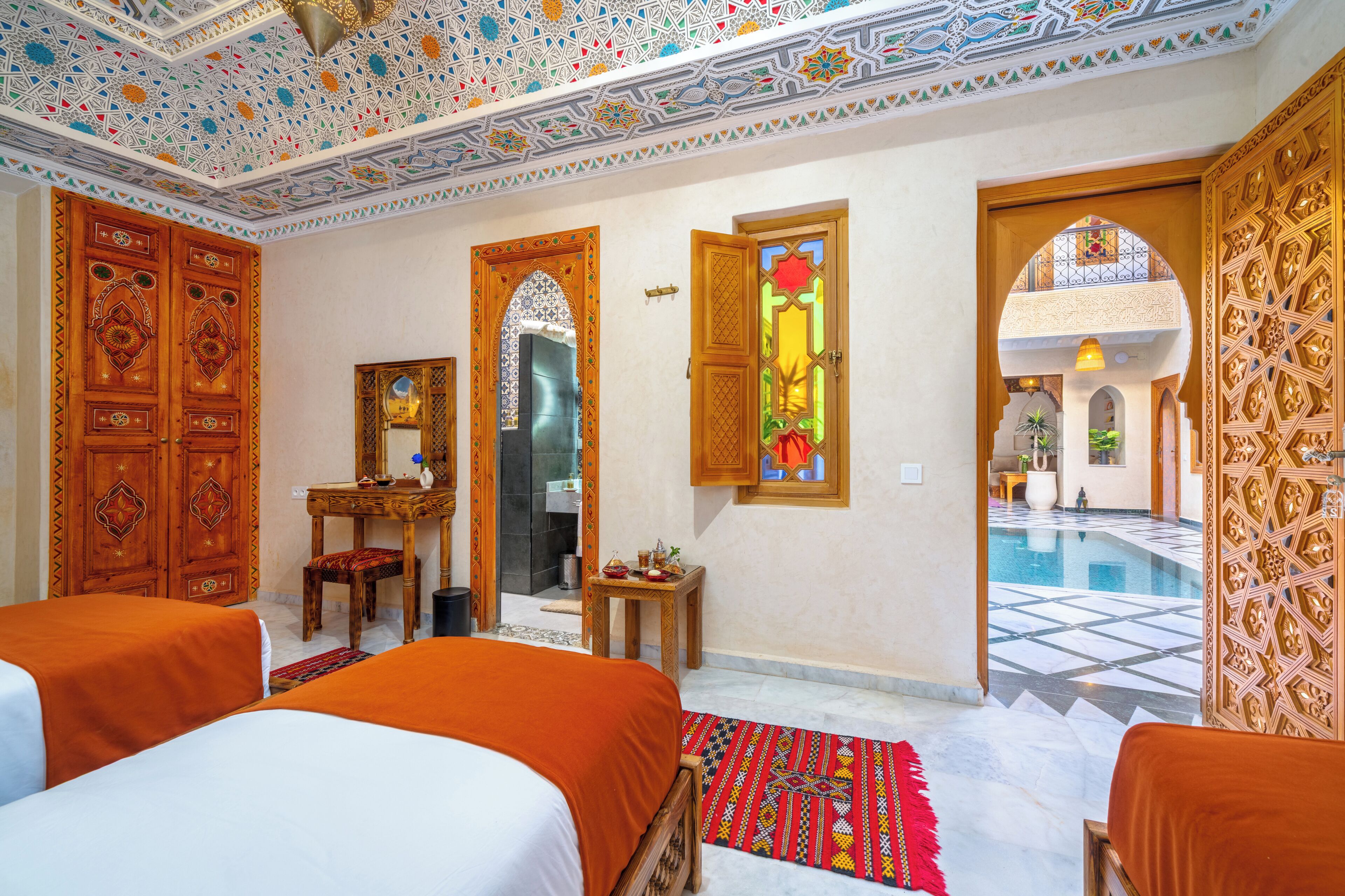 A hotel room with two beds, a desk, a mirror, and a view of a swimming pool.