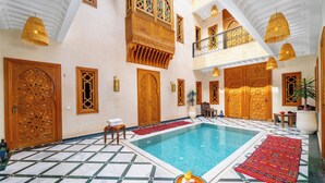 A luxurious indoor pool area with ornate wooden doors, a tiled floor, and hanging lights. - Riad Nadalinn (Marrakech)