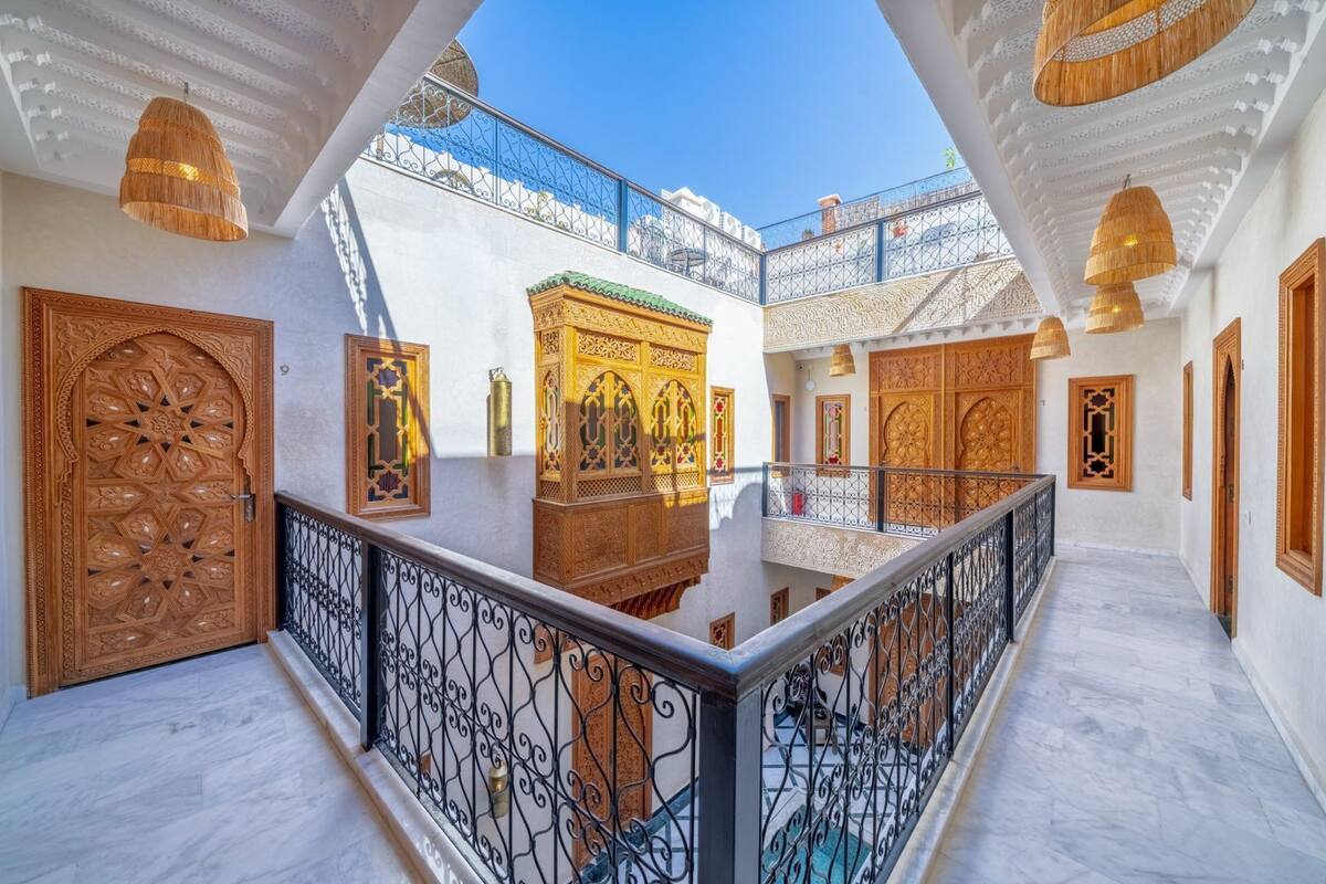 A courtyard with ornate wooden doors, a central decorative structure, and a balcony with wrought iron railings.